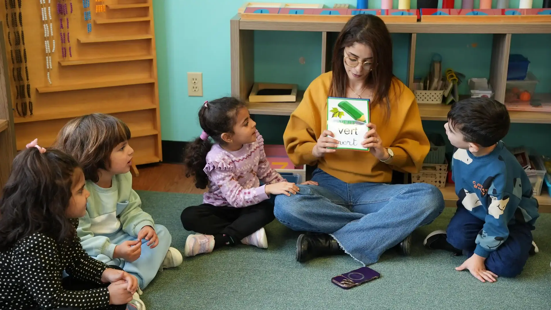 Teacher sitting on the carpet showing a vocabulary flashcard to a group of young children.